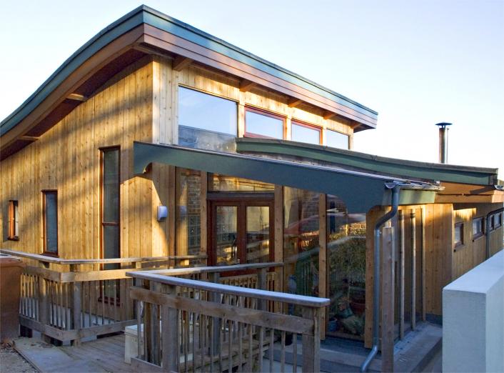 A timber clad straw bale house with curved roofs and high level glazing.